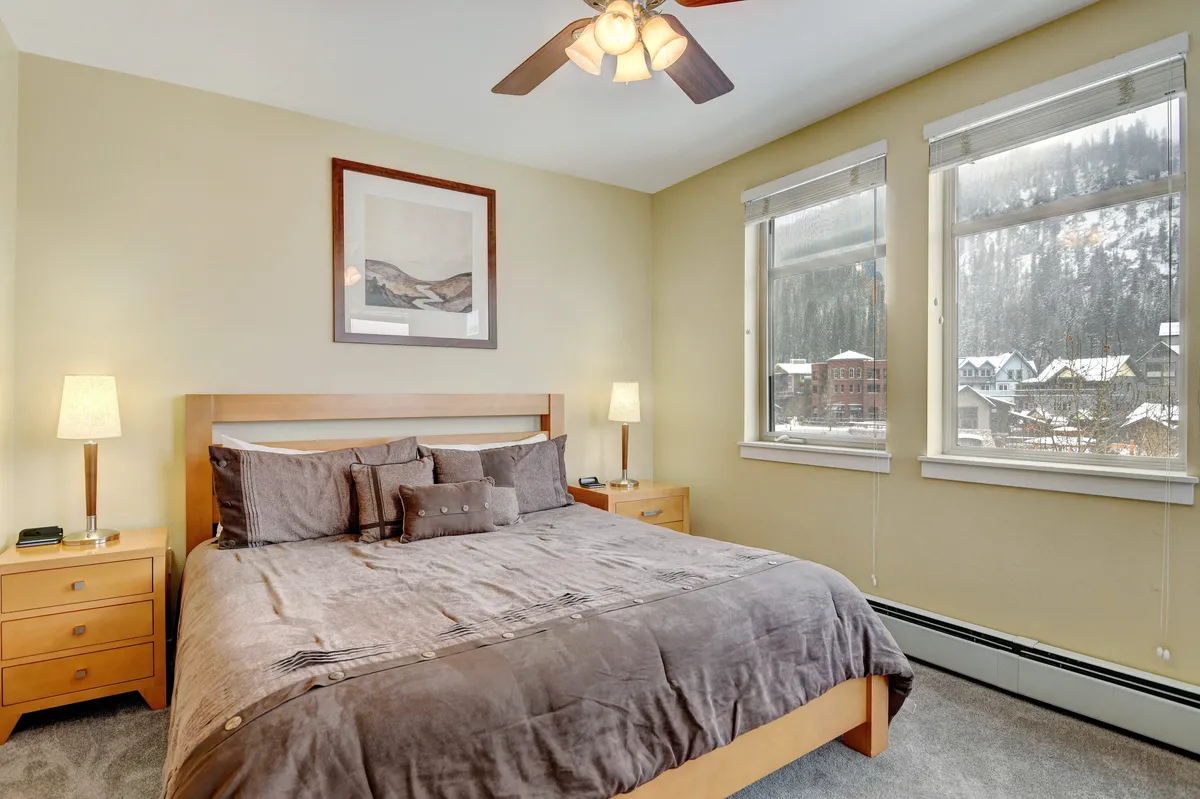 A serene and stylish bedroom featuring a plush bed with premium bedding, large windows letting in natural light, bedside tables with lamps, and tasteful wall art, creating a restful oasis perfect for unwinding at the end of the day.