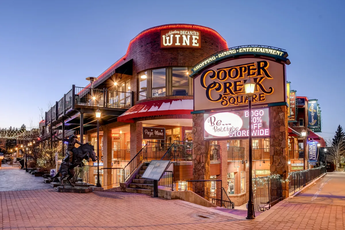 This image captures the exterior of Cooper Creek Square, featuring prominent signage, a wine shop sign, inviting outdoor seating, and a horse statue. The festive and welcoming atmosphere suggests a vibrant location where families can enjoy shopping, dining, and entertainment close to their lodgings.