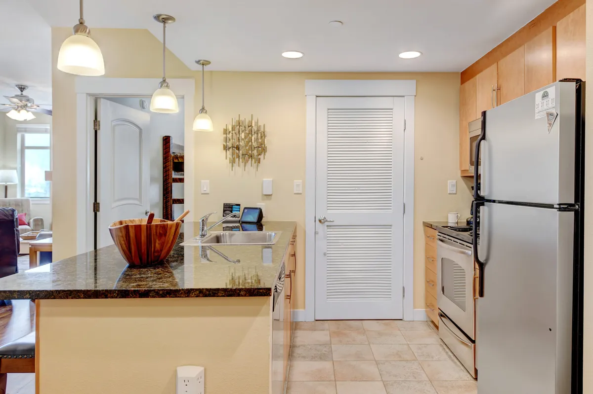 A welcoming, modern kitchen with granite countertops, a wooden bowl centerpiece, and stainless steel appliances. Pendant lighting illuminates the workspace, suggesting a space ready for both serious cooking and casual gatherings.