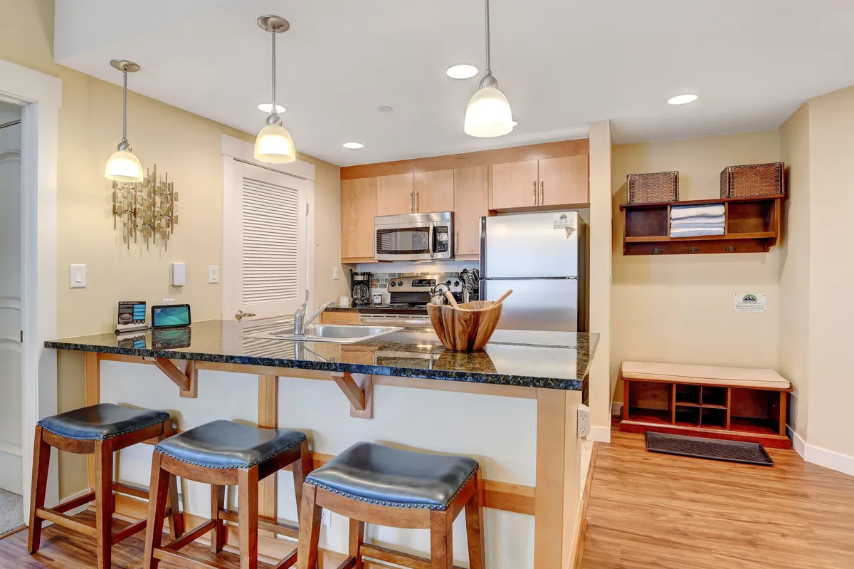 A cozy kitchen island with bar stools, featuring stainless steel appliances and a decorative bowl. The space exudes a sense of togetherness, ideal for casual breakfasts, snacks, or evening chats.