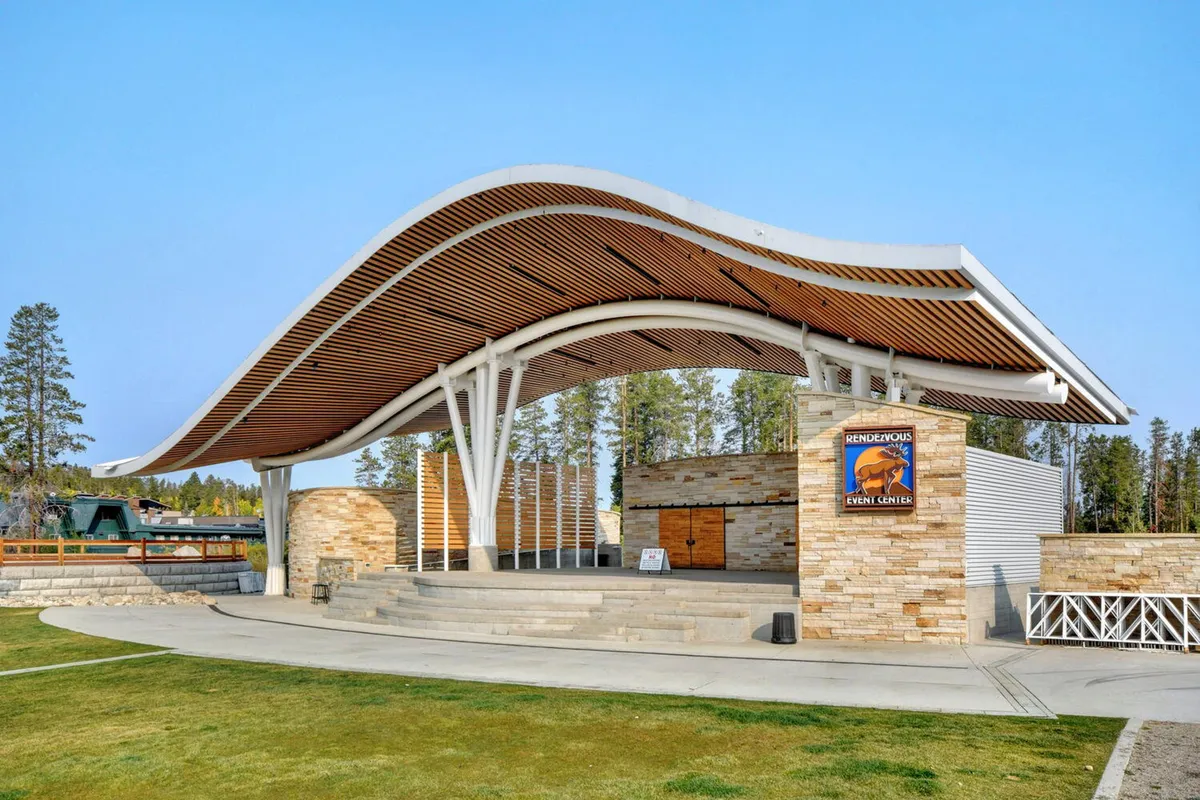 An exterior shot showcasing a modern curved-roof structure with a stone facade and open outdoor space. The setting is designed for community gatherings, outdoor performances, and festive events, inviting guests to explore beyond the accommodation itself.