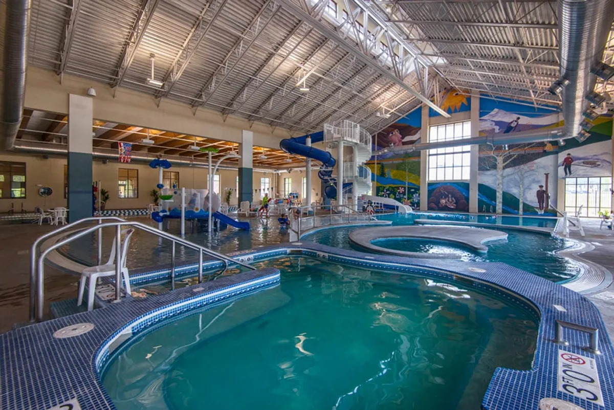 A lively indoor pool area featuring water slides, colorful murals, and children playing. The scene is full of energy, with families gathering and enjoying recreational activities together. The bright, engaging atmosphere highlights fun and relaxation for all ages.