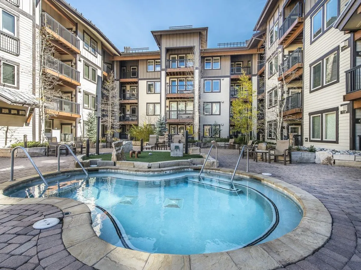 A serene exterior scene features a swimming pool framed by lush greenery and balconies, inviting guests to relax after a day of adventure. The atmosphere is tranquil but social, with spaces for both quiet reflection and gathering with friends or family.