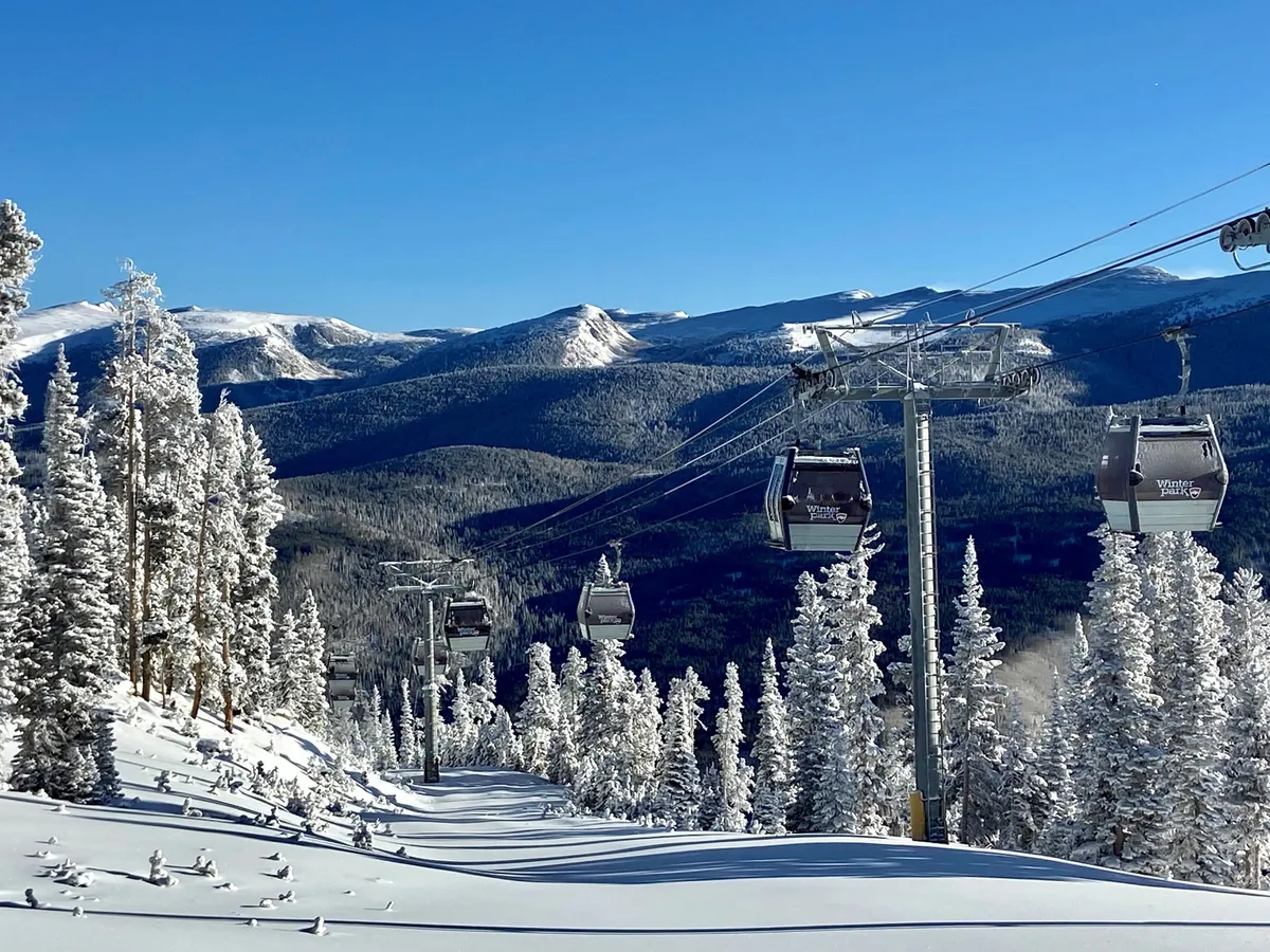 A striking exterior winter scene featuring ski gondolas gliding above snow-covered trees with a majestic mountain landscape as the backdrop. The image radiates serene winter adventure and the immediate accessibility of the slopes.