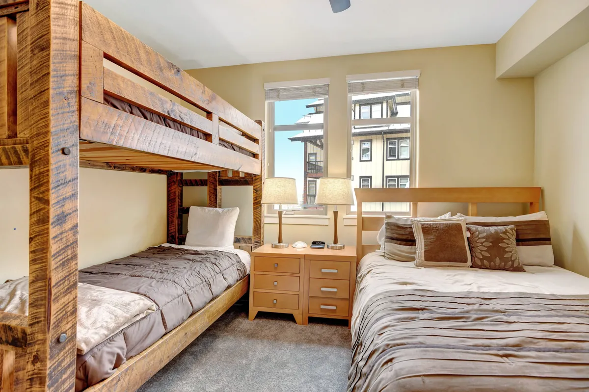 A welcoming family bedroom with a double bed and a bunk bed, flanked by a nightstand with a lamp. The space feels cozy and functional, ideal for flexible sleeping arrangements for families or groups.