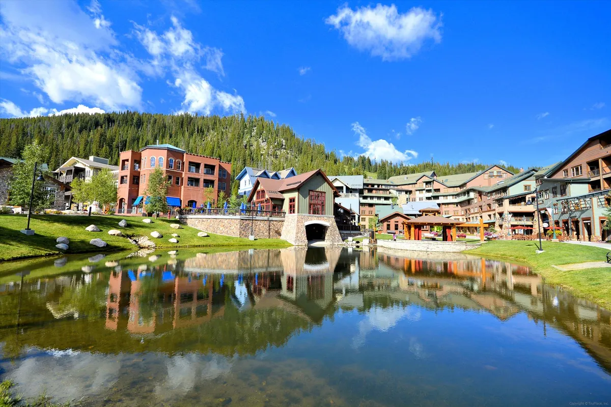 This serene scene shows a pond bordered by surrounding buildings and a charming bridge, with people enjoying walks, picnics, and possibly boating. The mood is peaceful yet communal, reflecting the area’s suitability for relaxed family outings and nature-based activities.