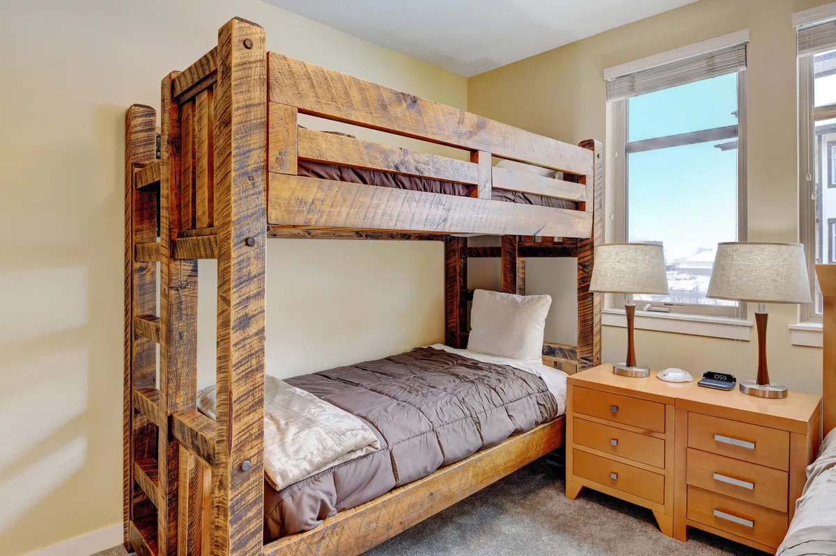A cheerful bedroom scene anchored by a bunk bed, nightstands, soft lamps, and large windows. The inviting arrangement suggests playful family moments and restful sleep after full days of adventure.